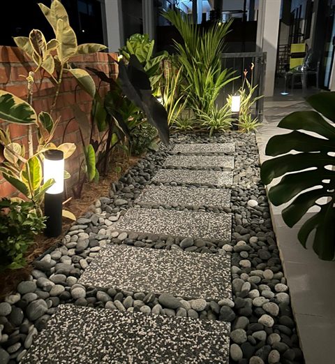 A lit side garden with a pebble path at night