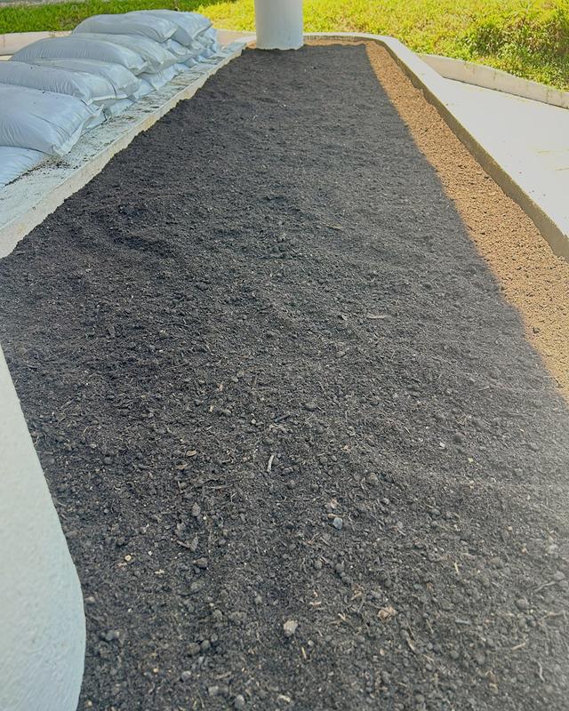 Curved concrete planter freshly filled and levelled with dark planting mix, soil bags stacked alongside