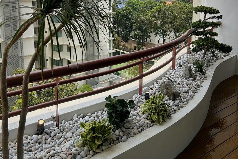 The curved planter from the other end: variegated foliage plants in white pebbles, rocks and the cloud-pruned tree at the far end.