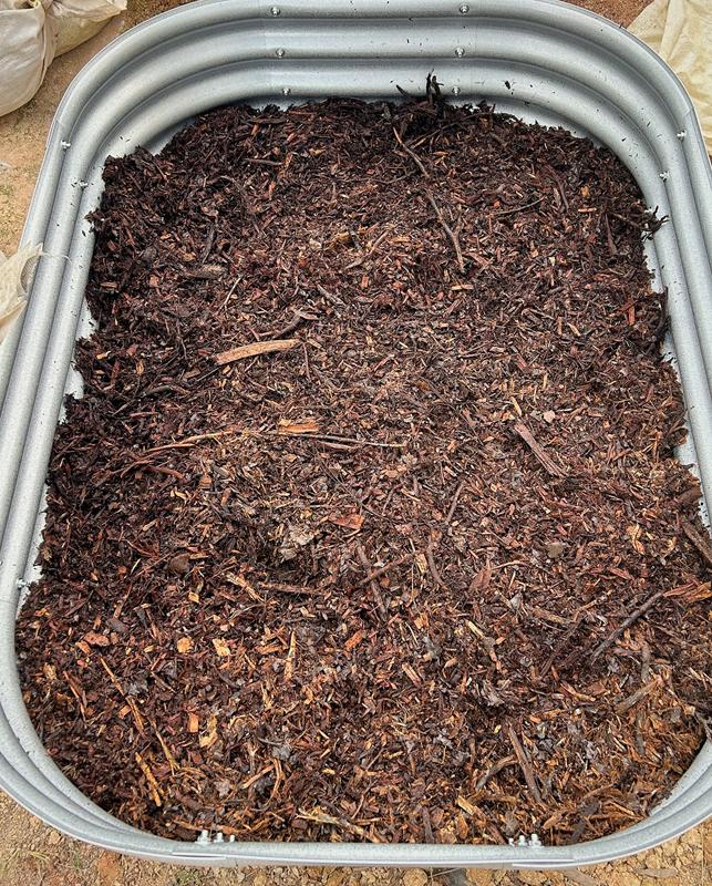 Top-down close-up of the dark, bark-rich organic mix inside a steel raised bed.